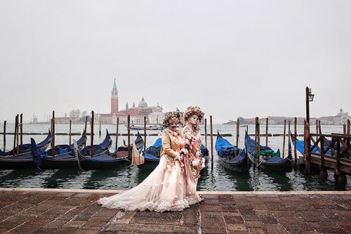 coppia con abiti e maschere veneziane lungo il canale della giudecca