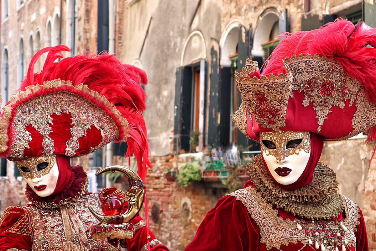 two people dressed up in carnival masks with red feathers
