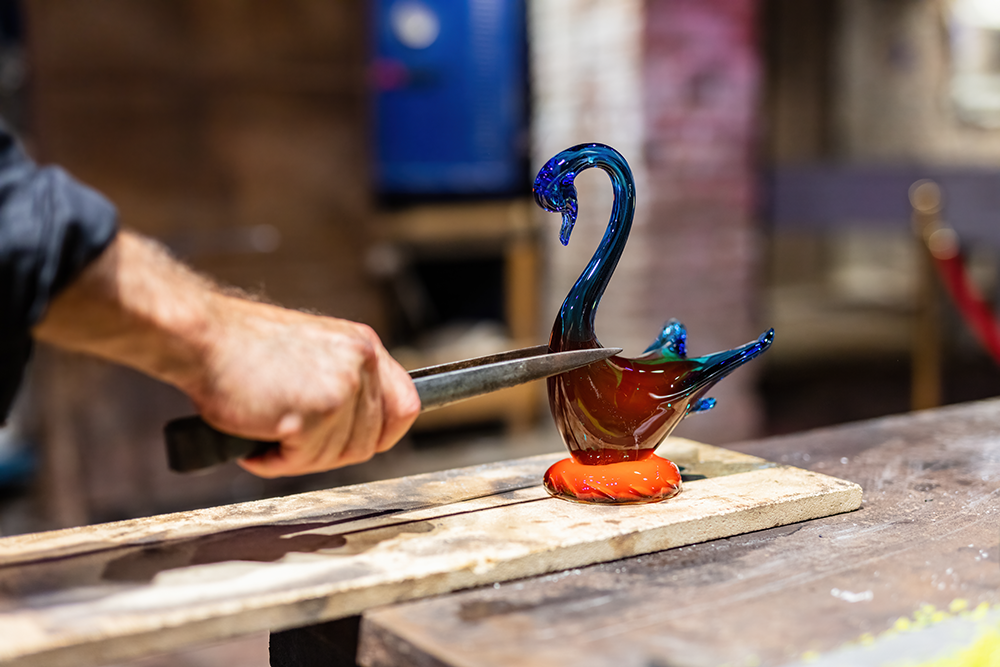 Close-up of traditional glassmaking in Murano, showing a craftsman shaping a colorful swan figure from molten glass