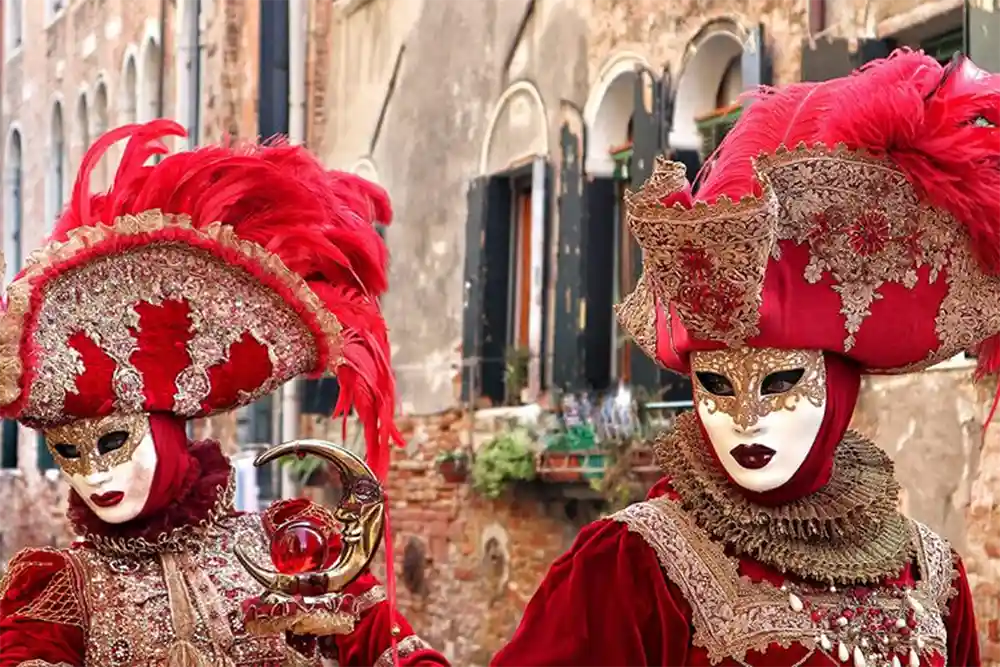Deux personnes masquées portant de riches costumes rouges avec des détails dorés pendant le Carnaval de Venise