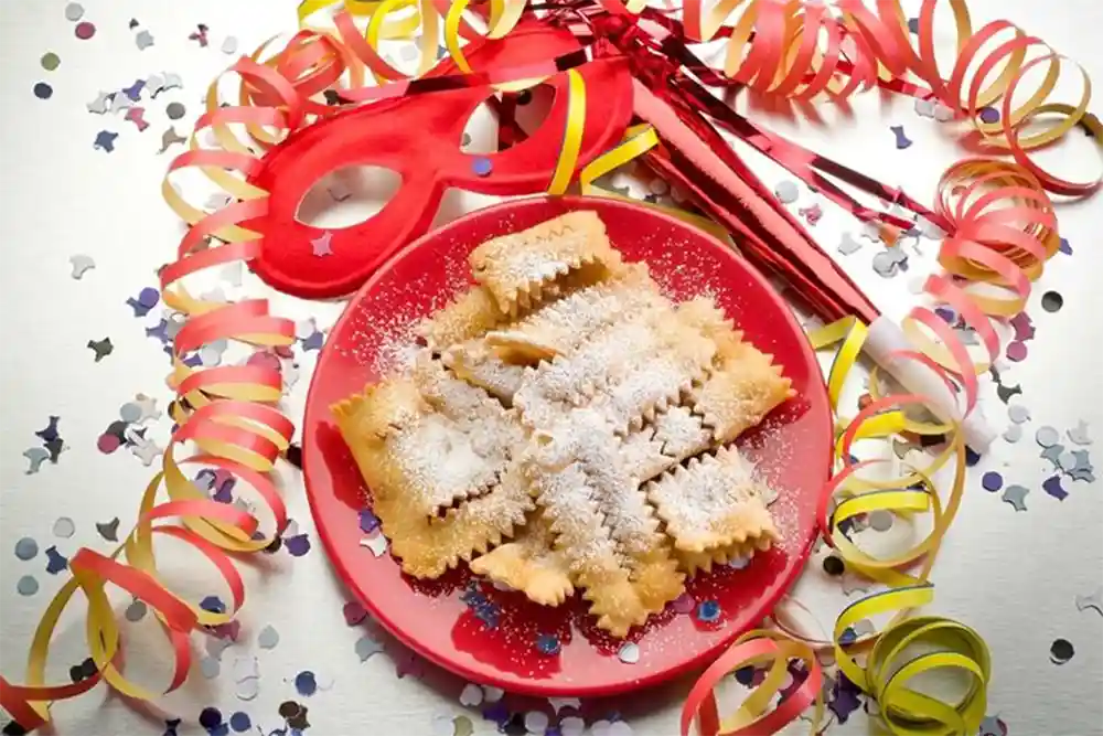 Dessert typique du carnaval, chiacchiere, servi sur une assiette rouge et entouré de confettis et de banderoles colorées