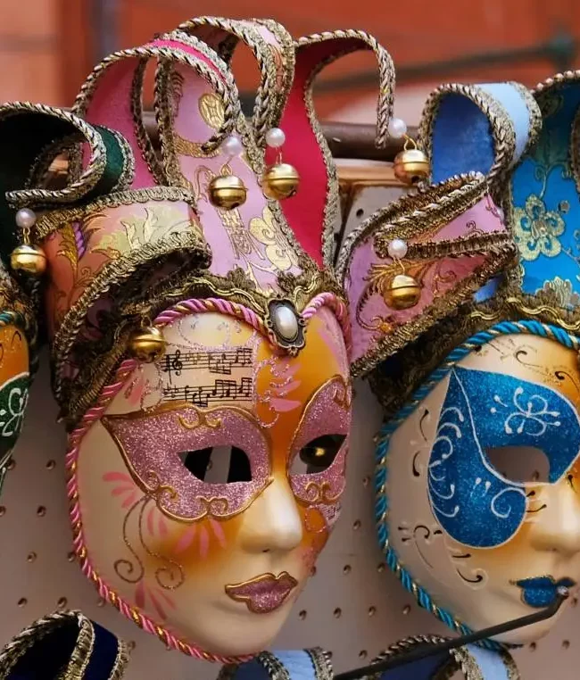 Primer plano de una serie de máscaras venecianas tradicionales a la venta, todas decoradas con patrones brillantes y coloridos.