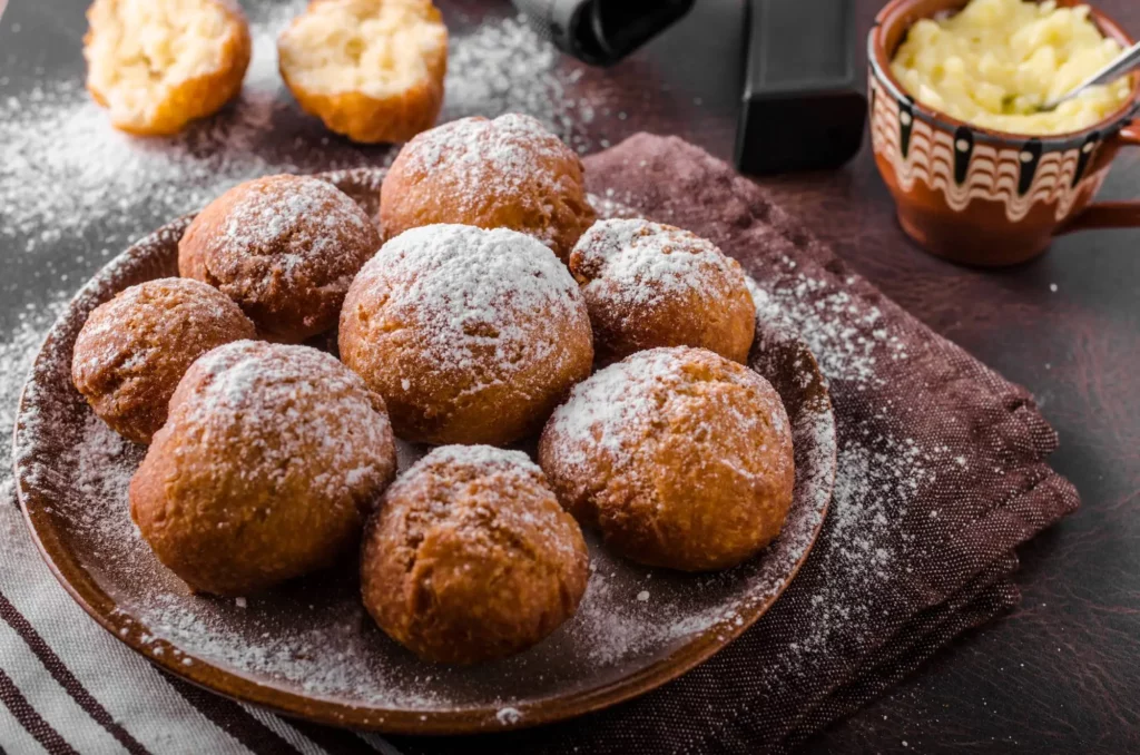 Frittelle veneziane con zucchero a velo servite su un piatto di ceramica scura.