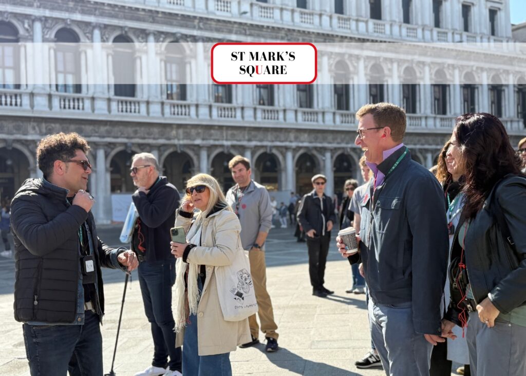 Group of tourists on a guided tour in St. Mark’s Square with a local guide and historic buildings in the background