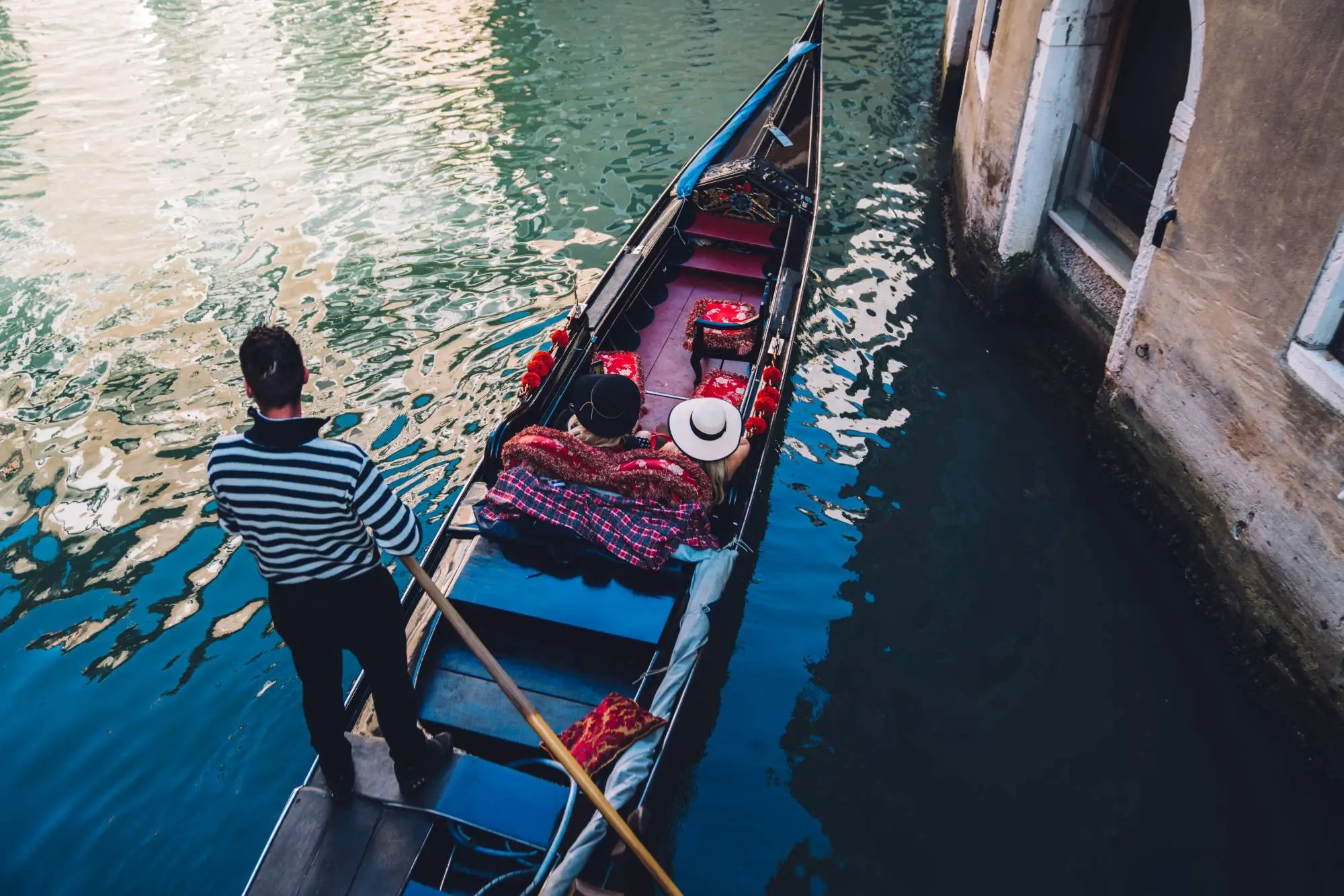 Gondolier steering a traditional gondola with two passengers along a quiet Venetian canal